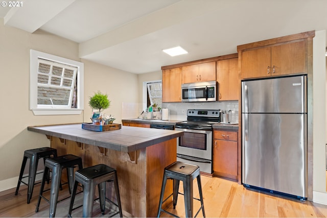 kitchen featuring tile counters, stainless steel appliances, light hardwood / wood-style flooring, decorative backsplash, and a kitchen bar