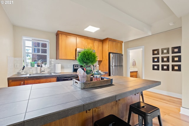 kitchen with tasteful backsplash, light wood-type flooring, dishwasher, stainless steel fridge, and sink