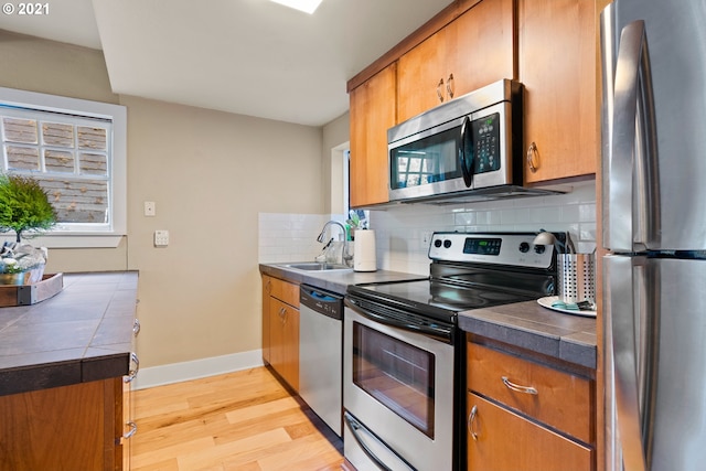 kitchen with light wood-type flooring, tile counters, stainless steel appliances, sink, and decorative backsplash