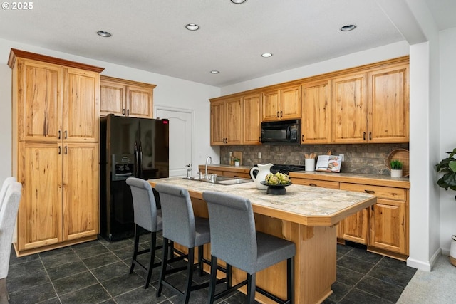 kitchen with a sink, backsplash, black appliances, and a kitchen island with sink