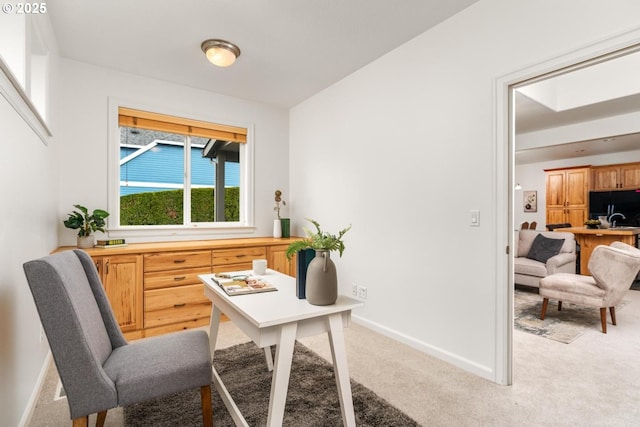 office area featuring baseboards and light carpet