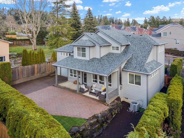 rear view of property featuring outdoor lounge area, fence, driveway, and roof with shingles