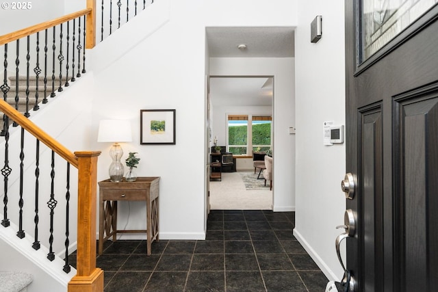 foyer with stairs, baseboards, and dark colored carpet