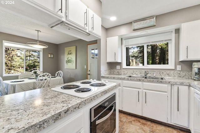 kitchen featuring black oven, white electric cooktop, pendant lighting, and white cabinets