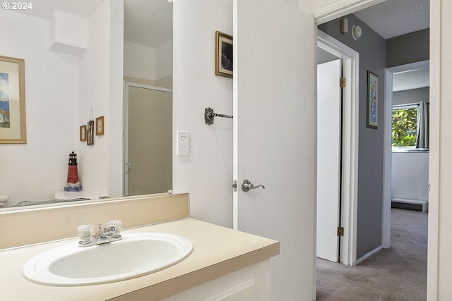 bathroom featuring a shower with shower door, vanity, and a textured ceiling