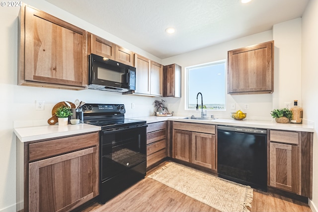 kitchen featuring sink, black appliances, a textured ceiling, and light hardwood / wood-style floors