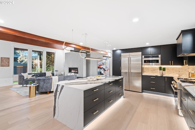 kitchen featuring light wood-type flooring, a fireplace, a kitchen island, high quality appliances, and pendant lighting