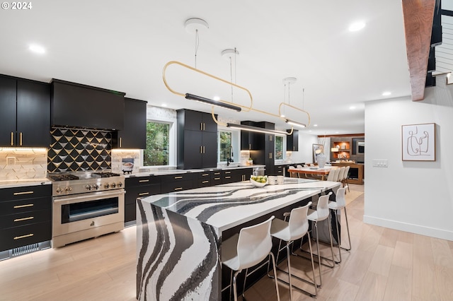 kitchen with hanging light fixtures, backsplash, stainless steel stove, light wood-type flooring, and sink