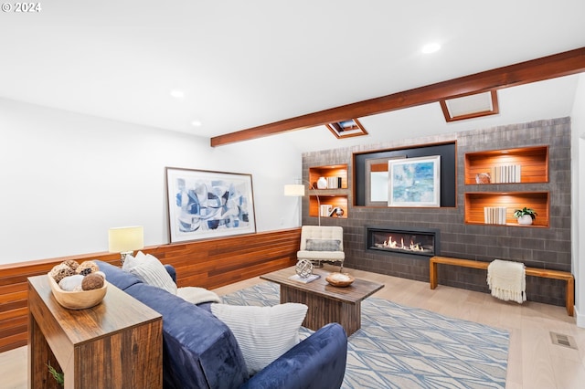 living room with a fireplace, beamed ceiling, and light wood-type flooring