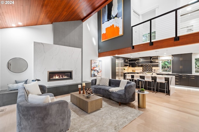 living room with wood ceiling, high vaulted ceiling, light wood-type flooring, and a high end fireplace