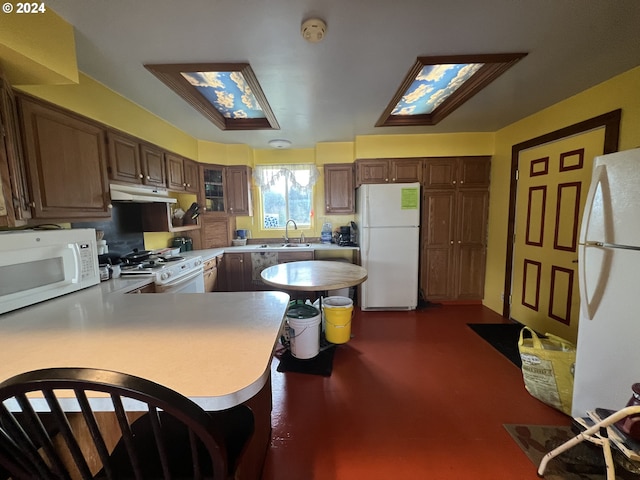 kitchen featuring under cabinet range hood, a peninsula, white appliances, a sink, and glass insert cabinets