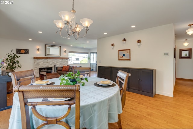 dining space with a chandelier, a stone fireplace, and light hardwood / wood-style floors