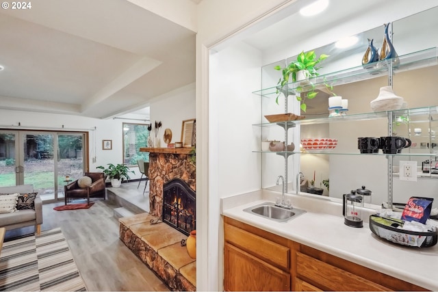 bar featuring sink, hanging light fixtures, a fireplace, a tray ceiling, and light hardwood / wood-style floors