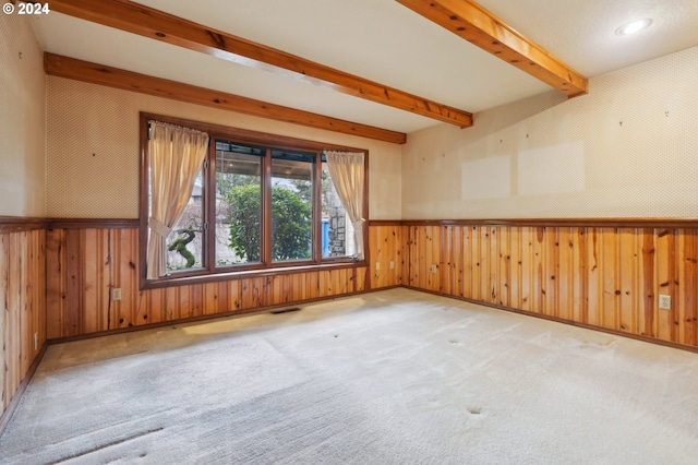 empty room featuring beamed ceiling, light colored carpet, and wooden walls