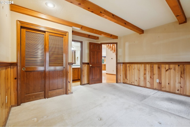 interior space featuring beamed ceiling, light carpet, and wooden walls