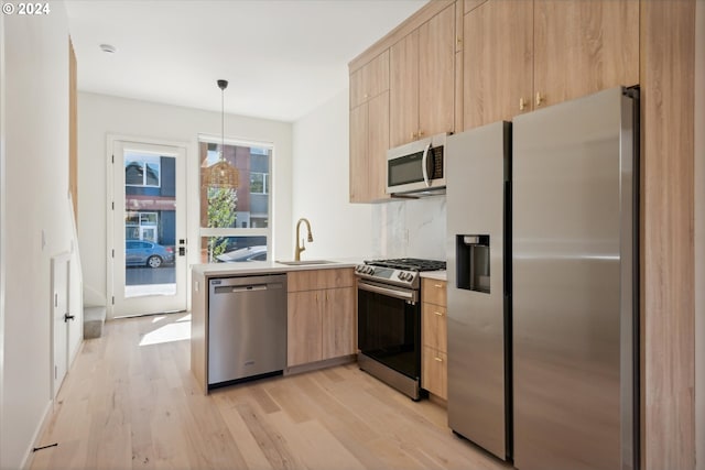 kitchen featuring light brown cabinets, sink, decorative light fixtures, stainless steel appliances, and light hardwood / wood-style flooring