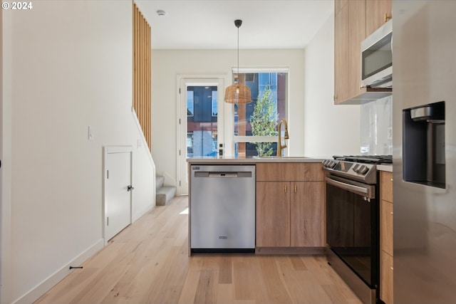 kitchen with appliances with stainless steel finishes, sink, light hardwood / wood-style floors, and hanging light fixtures