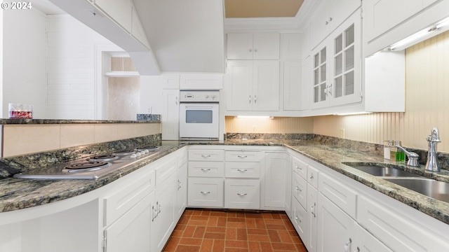 kitchen with stainless steel gas cooktop, sink, dark stone countertops, white cabinets, and oven