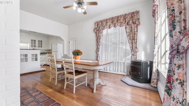 dining space with a wood stove, light wood finished floors, and ceiling fan