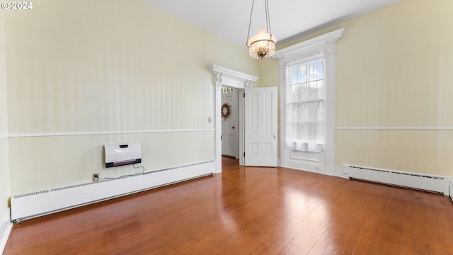 empty room with a chandelier, hardwood / wood-style flooring, and baseboard heating