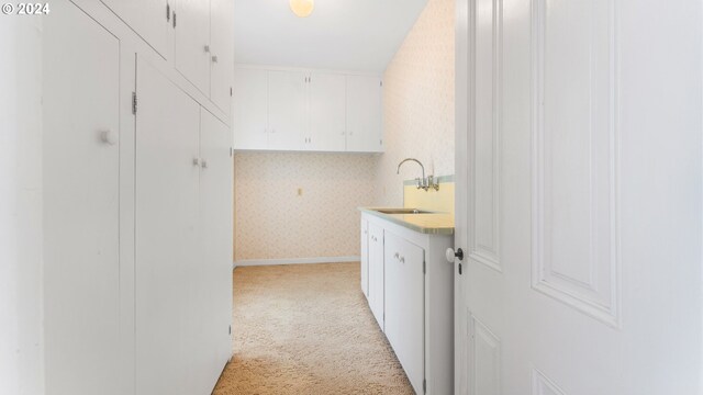 clothes washing area featuring light colored carpet, wallpapered walls, and a sink