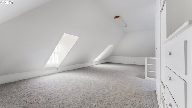 additional living space with vaulted ceiling with skylight and light colored carpet