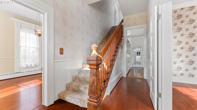 staircase with wallpapered walls, hardwood / wood-style floors, wainscoting, and a baseboard heating unit