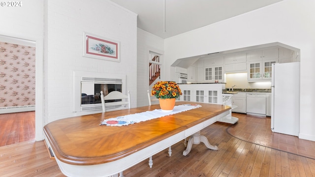 dining area with baseboard heating, sink, a fireplace, and hardwood / wood-style flooring