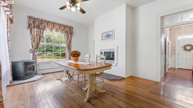 dining space featuring a wood stove, ceiling fan, a baseboard radiator, and hardwood / wood-style flooring