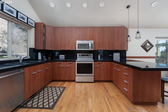 kitchen featuring a kitchen breakfast bar, decorative light fixtures, appliances with stainless steel finishes, and light wood-type flooring