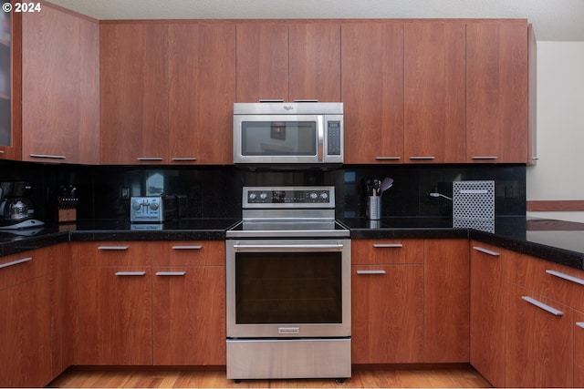 kitchen featuring light wood-type flooring, stainless steel appliances, decorative backsplash, and dark stone countertops