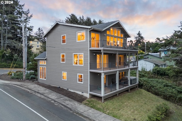 back house at dusk featuring a lawn and a balcony