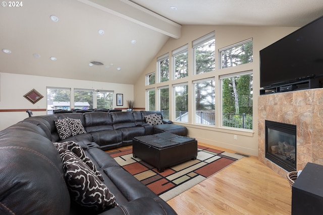 living room featuring beam ceiling, a tile fireplace, a healthy amount of sunlight, and light hardwood / wood-style flooring