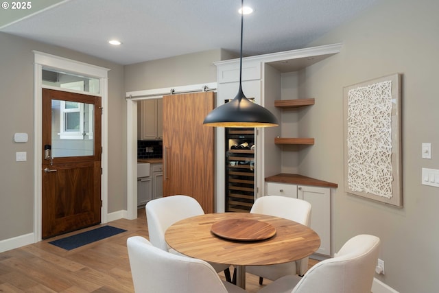 dining area with a textured ceiling, wine cooler, a barn door, and light hardwood / wood-style flooring