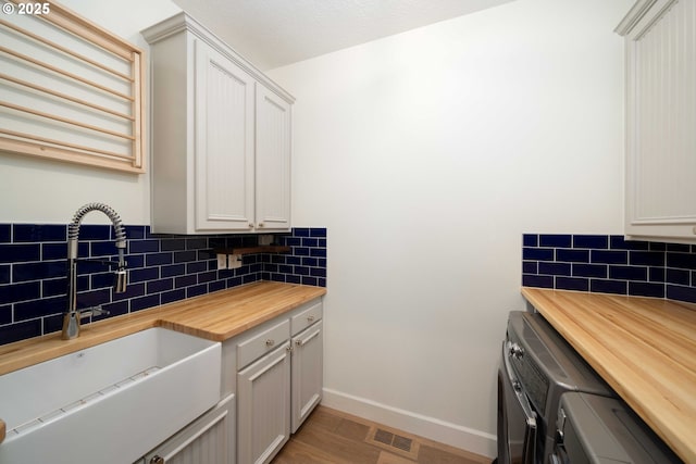 kitchen with backsplash, washer and dryer, sink, light wood-type flooring, and butcher block counters