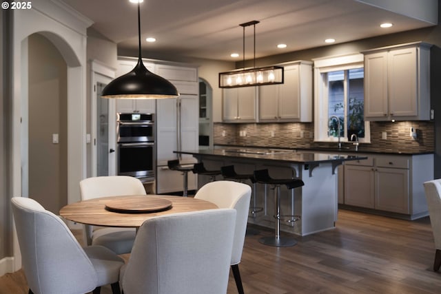 kitchen featuring stainless steel double oven, a kitchen island, dark wood-type flooring, hanging light fixtures, and a breakfast bar area