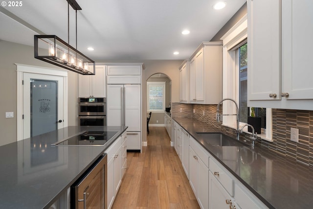 kitchen with pendant lighting, sink, white cabinets, beverage cooler, and paneled built in refrigerator