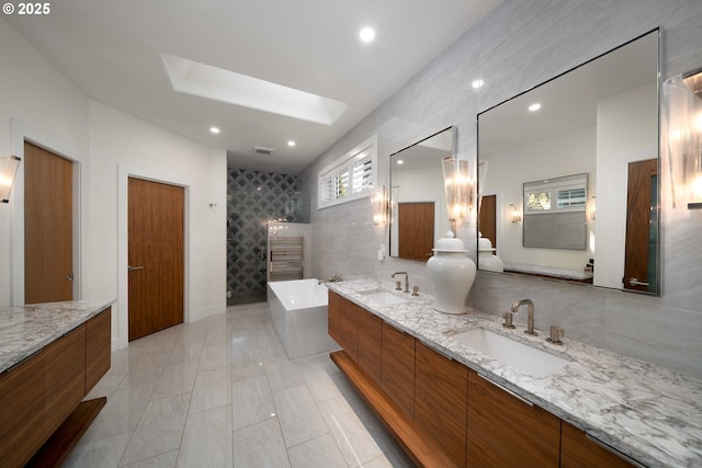 bathroom with tile walls, vanity, a skylight, and independent shower and bath