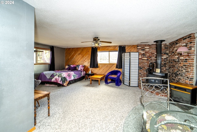 bedroom with carpet, a textured ceiling, ceiling fan, a wood stove, and wood walls