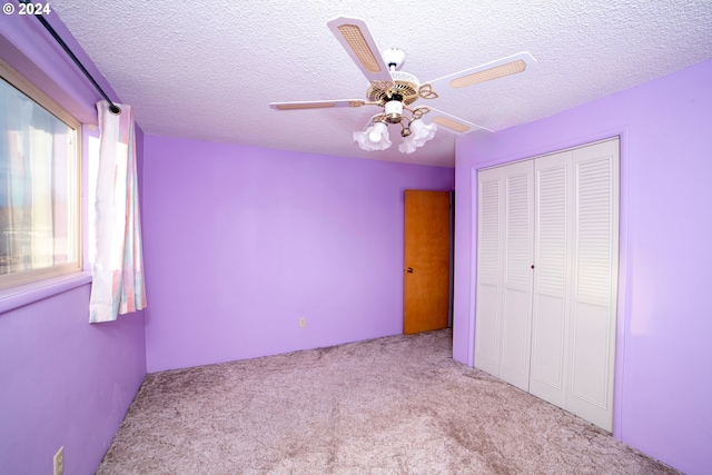 unfurnished bedroom featuring ceiling fan, light colored carpet, a textured ceiling, and a closet