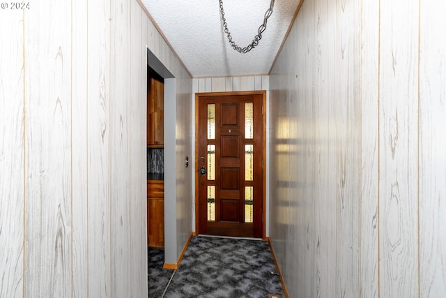 doorway to outside with dark colored carpet, a textured ceiling, and wood walls