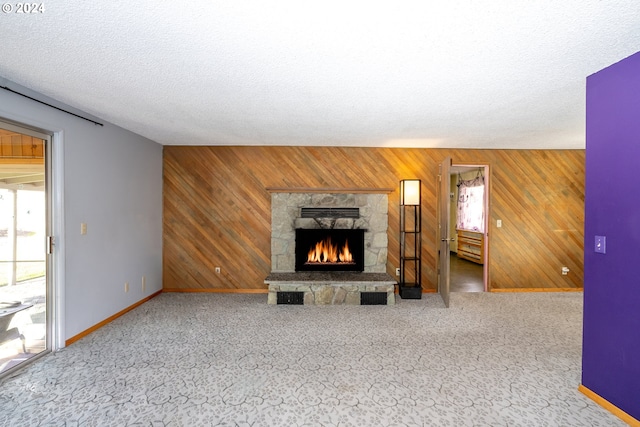 unfurnished living room featuring carpet, a fireplace, wooden walls, and a textured ceiling