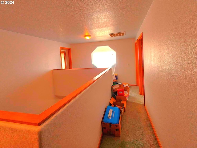 corridor with carpet floors, visible vents, a textured wall, a textured ceiling, and baseboards