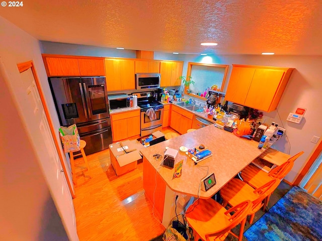 kitchen with light wood finished floors, stainless steel appliances, a sink, a textured ceiling, and a peninsula