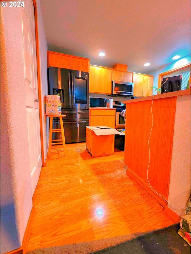 kitchen featuring kitchen peninsula, a kitchen breakfast bar, light wood-type flooring, black appliances, and a kitchen island