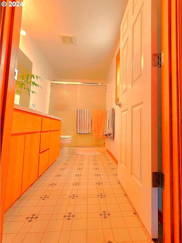 bathroom featuring tile patterned floors, vanity, a shower with shower door, and toilet