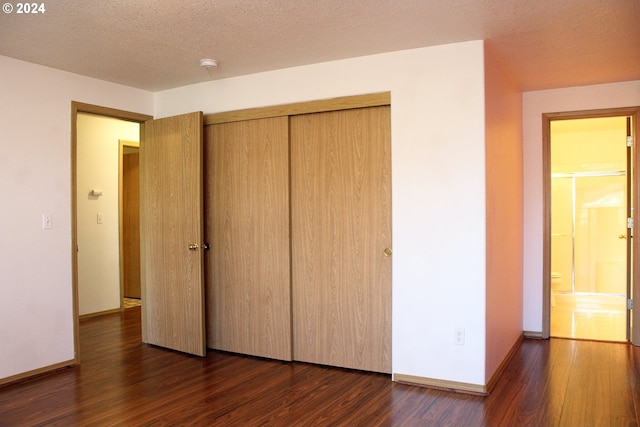 unfurnished bedroom with a textured ceiling, dark hardwood / wood-style floors, and a closet