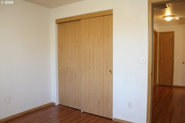 unfurnished bedroom featuring a textured ceiling, dark wood-type flooring, and a closet