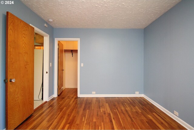 unfurnished bedroom featuring hardwood / wood-style flooring, a walk in closet, a textured ceiling, and a closet