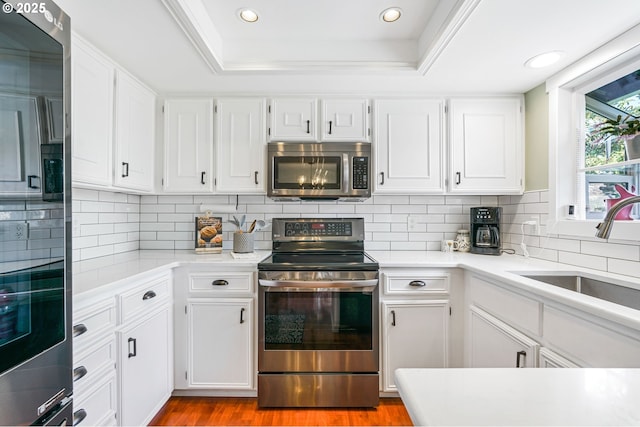 kitchen with stainless steel appliances, a tray ceiling, a sink, and light countertops